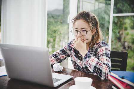 woman sitting down, his face unsettled. At the computer desk she has headaches and stress. Cause of hard work and insufficient rest.の写真素材