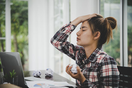 woman sitting down, his face unsettled. At the computer desk she has headaches and stress. Cause of hard work and insufficient rest.の写真素材