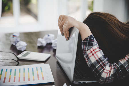 Tired businesswoman working on a computer Portrait of stressed young woman comfortably with headache at desk. Exhausted business woman working on laptop at office.の写真素材