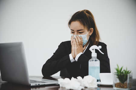 Sick young asian business woman wearing protective face mask having cold fever.Health problems conceptの写真素材