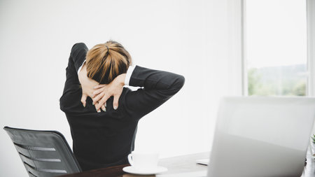 Young asian business woman sitting on the chair twisted relieve fatigue  while she is sitting in the office workingの写真素材