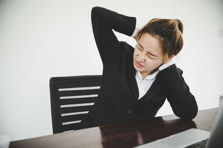 Young asian woman is sitting at work and has pain in her neck while she is sitting in the office workingの写真素材