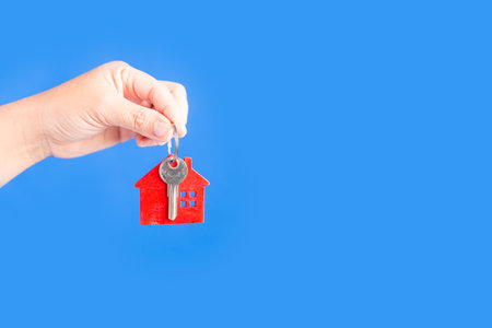 Woman hand holding key house on blue backgroundの写真素材