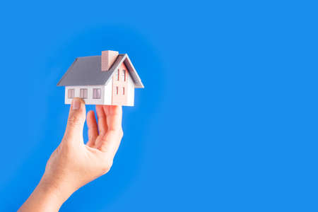 Female hands holding small model house on blue backgroundの写真素材