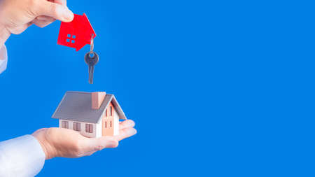 Female hands holding little model house with key  on blue background