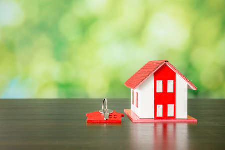 Small model house with key against green bokeh background. building, loan, real estate or buying a new home concept.の写真素材