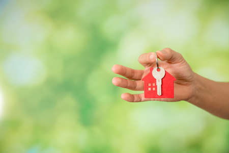 Small model house with key against green bokeh background. building, loan, real estate or buying a new home concept.の写真素材