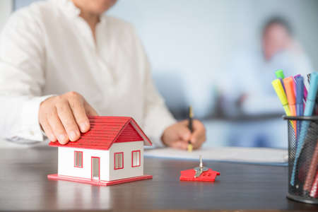 Businesswoman choosing mini house model from model on wood table, Planning to buy property. concept of Choose the best.の写真素材