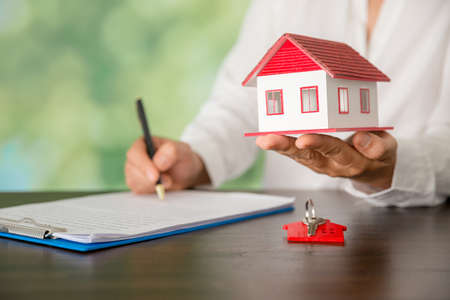 Small model house with key against green bokeh background. building, loan, real estate or buying a new home concept.の写真素材