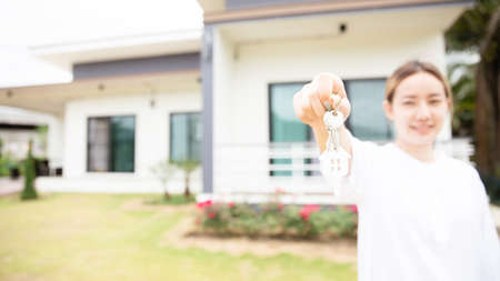 Close up portrait of smiling asian woman hold show keys in front of new house. estate and property conceptの写真素材