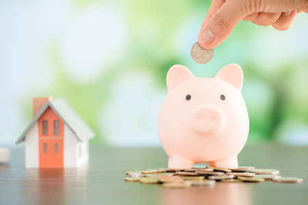 Hand putting coin in a piggy bank. Saving money concept to buy a house.の写真素材