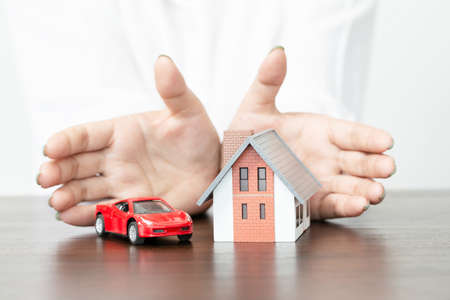 young woman use two hand to protect house model and toy car. real estate, insurance and property conceptsの写真素材