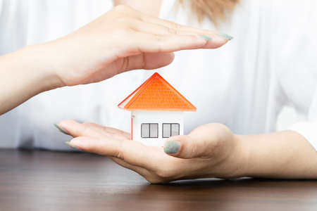 Hands of a woman surround a house model. real estate, insurance and property conceptsの写真素材