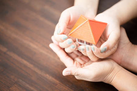 Male and female hands hold a small house. Concept of real estate and family homeの写真素材
