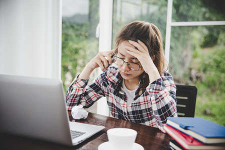 Tired businesswoman working on a computer Portrait of stressed young woman comfortably with headache at desk. Exhausted business woman working on laptop at office.の写真素材