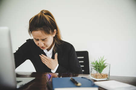 Asian businesswoman  in a black suit is sick with chest pain while sitting at work.Heart Attack, Chest Pain, Womenの写真素材