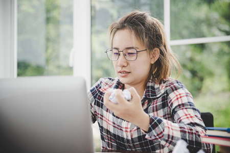 woman sitting down, his face unsettled. At the computer desk she has headaches and stress. Cause of hard work and insufficient rest.の写真素材