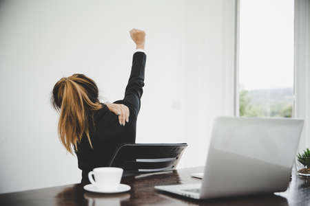 Young asian woman are tired from work, sit in a chair, stretch and massage arm, shoulder For relaxation while while she is sitting in the office workingの写真素材
