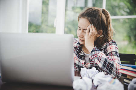 woman sitting down, his face unsettled. At the computer desk she has headaches and stress. Cause of hard work and insufficient rest.の写真素材