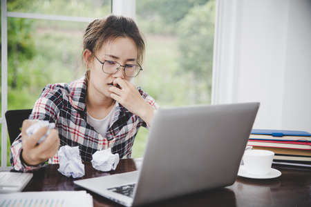 woman sitting down, his face unsettled. At the computer desk she has headaches and stress. Cause of hard work and insufficient rest.の写真素材