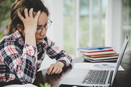 woman sitting down, his face unsettled. At the computer desk she has headaches and stress. Cause of hard work and insufficient rest.の写真素材
