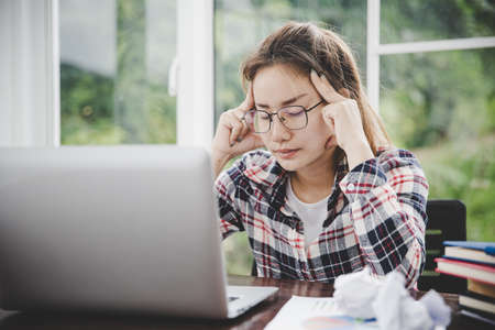 woman sitting down, his face unsettled. At the computer desk she has headaches and stress. Cause of hard work and insufficient rest.の写真素材