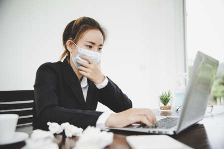 Sick young asian business woman wearing protective face mask having cold fever.Health problems conceptの写真素材