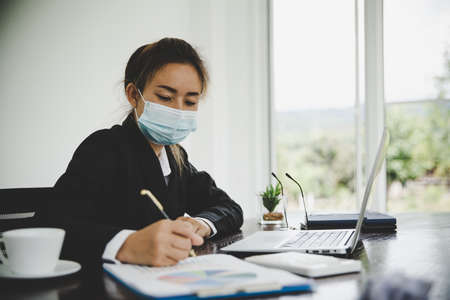 asian business woman wearing facial mask working on laptop in business office, new normal due to   outbreakの写真素材