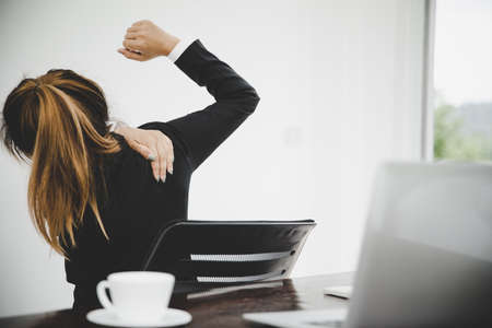 Young asian woman are tired from work, sit in a chair, stretch and massage arm, shoulder For relaxation while while she is sitting in the office workingの写真素材