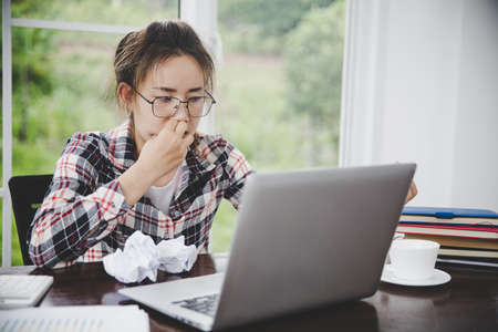 woman sitting down, his face unsettled. At the computer desk she has headaches and stress. Cause of hard work and insufficient rest.の写真素材