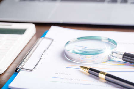 magnifying glass with business document financial paper chart statistic report on desk in office, closeup calculating machine with paperwork on table concept for analysis, market, bankingの写真素材