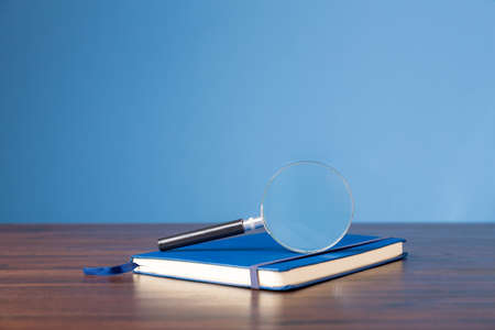 Not book with magnifying glass on wooden desk in information library of school or university, concept for education, reading , study, copy space and blue background.の写真素材