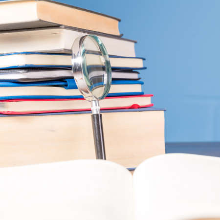 Stack book with magnifying glass on wooden desk in information library of school or university, concept for education, reading, study, copy space on blue background.の写真素材