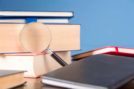 Stack book with magnifying glass on wooden desk in information library of school or university, concept for education, reading, study, copy space on blue background.の写真素材