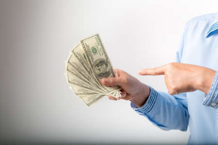 I'm rich! Portrait of successful happy woman with fancy brown hair pointing to dollar bills, showing money and boasting lottery winning, big profit. indoor studio shot isolated on gray backgroundの写真素材