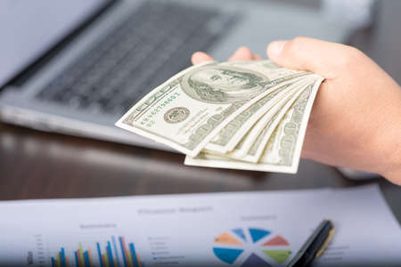 Close up young business woman using counting cash money one hundred dollar bills, checking financial documents, sitting at table with papers and tax form, managing planning budget, accounting expensesの写真素材