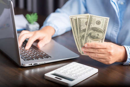 Close up young business woman using counting cash money one hundred dollar bills, checking financial documents, sitting at table with papers and tax form, managing planning budget, accounting expensesの写真素材