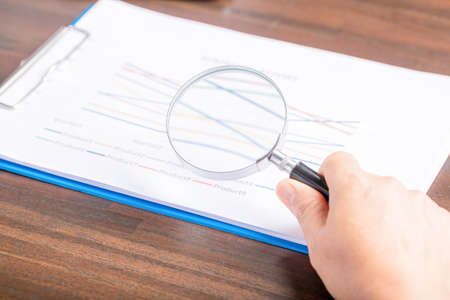 professional business woman hand holding and using magnifying glass search finance document paper on desk in office, businesswoman looking at data with analyzing statisticsの写真素材