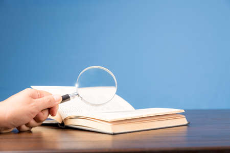 open book with magnifying glass on wooden desk in information library of school or university, concept for education,reading , study, copy space and blue background.の写真素材