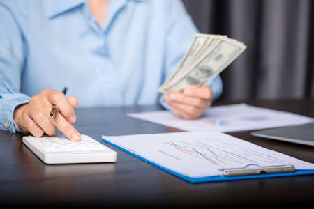 Close up young business woman using counting cash money one hundred dollar bills, checking financial documents, sitting at table with papers and tax form, managing planning budget, accounting expensesの写真素材
