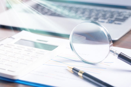 magnifying glass with business document financial paper chart statistic report on desk in office, closeup calculating machine with paperwork on table concept for analysis, market, bankingの写真素材