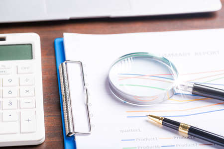 magnifying glass with business document financial paper chart statistic report on desk in office, closeup calculating machine with paperwork on table concept for analysis, market, bankingの写真素材