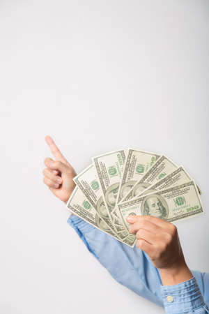 Close up woman holding dollars happy pointing with hand and finger to the side successful, showing money and boasting lottery winning, big profit. indoor studio shot isolated on gray backgroundの写真素材