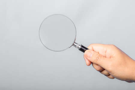 woman hand holding magnifying glass isolated on gray background. optical zoom lens is macro tool, concept for education, science.の写真素材