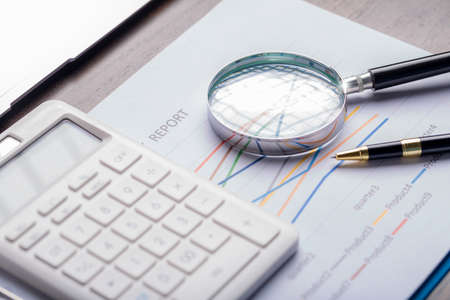 magnifying glass with business document financial paper chart statistic report on desk in office,...