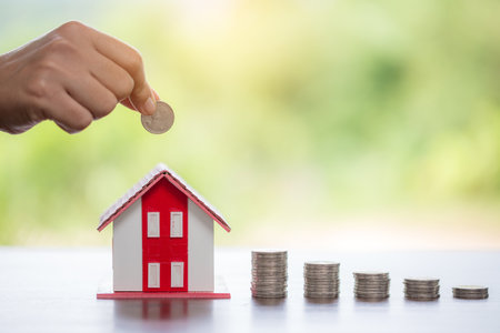 Hand putting coin in house model of coin for saving money for buying house. Savings plans for home, loan, investment, mortgage, finance and banking about house concept.の写真素材