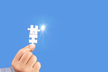 Hands holding jigsaw puzzles piece with clear blue background, success business, solution strategy, teamwork partnership conceptの写真素材