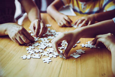 Hands of a person little child and parent playing jigsaw puzzle piece game together on wooden table at home, concept for leisure with family, play with children's development, education and fun.の写真素材