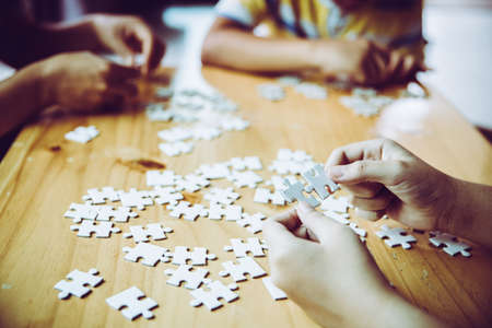 Hands of a person little child and parent playing jigsaw puzzle piece game together on wooden table at home, concept for leisure with family, play with children's development, education and fun.の写真素材