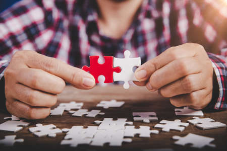 Hands holding jigsaw puzzles piece on wooden table background, success business, solution strategy, teamwork partnership conceptの写真素材